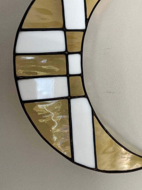 Decorative stained glass moon shape held by a hand on a plain background
